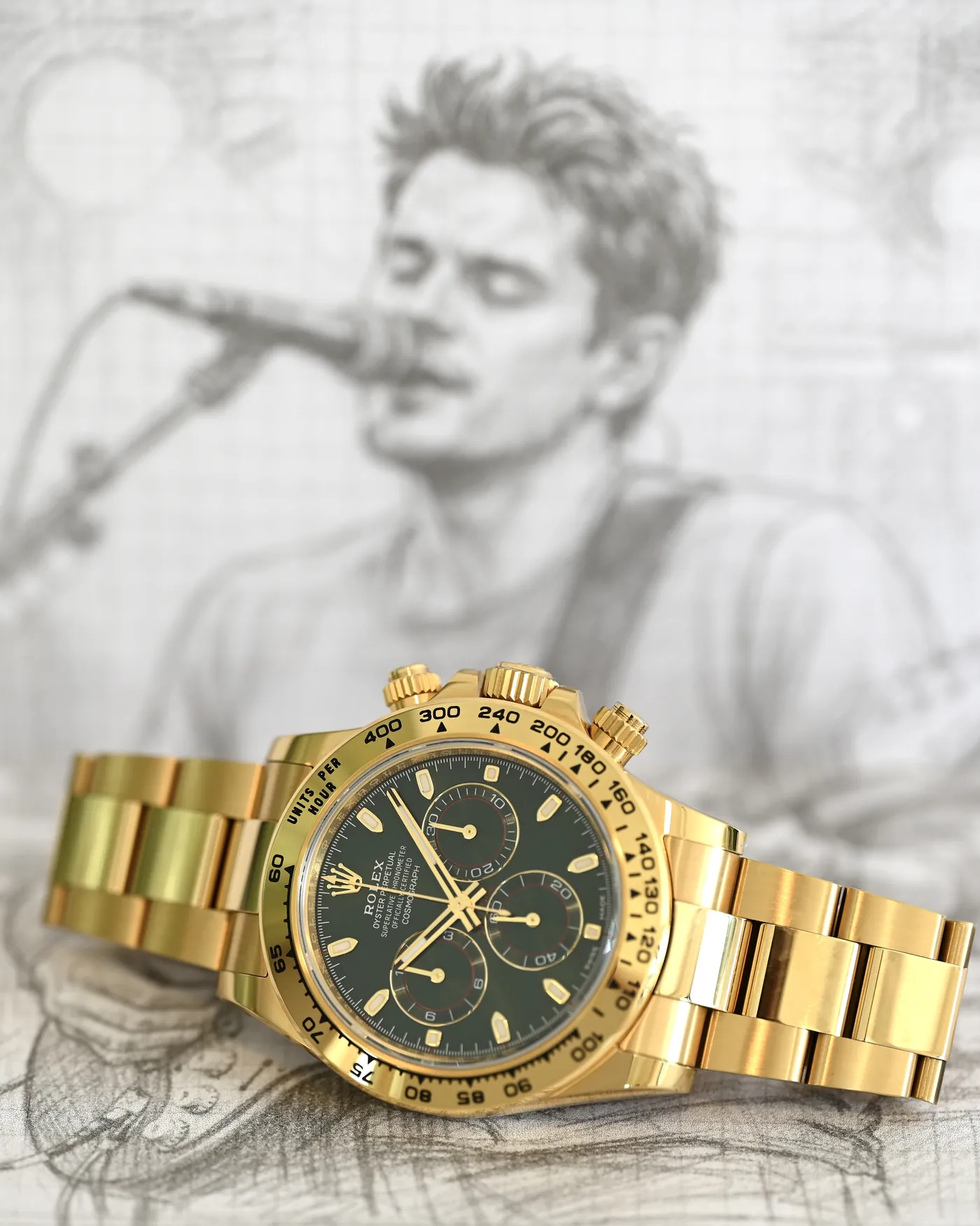 Yellow-gold Daytona with green dial resting in front of a pencil sketch